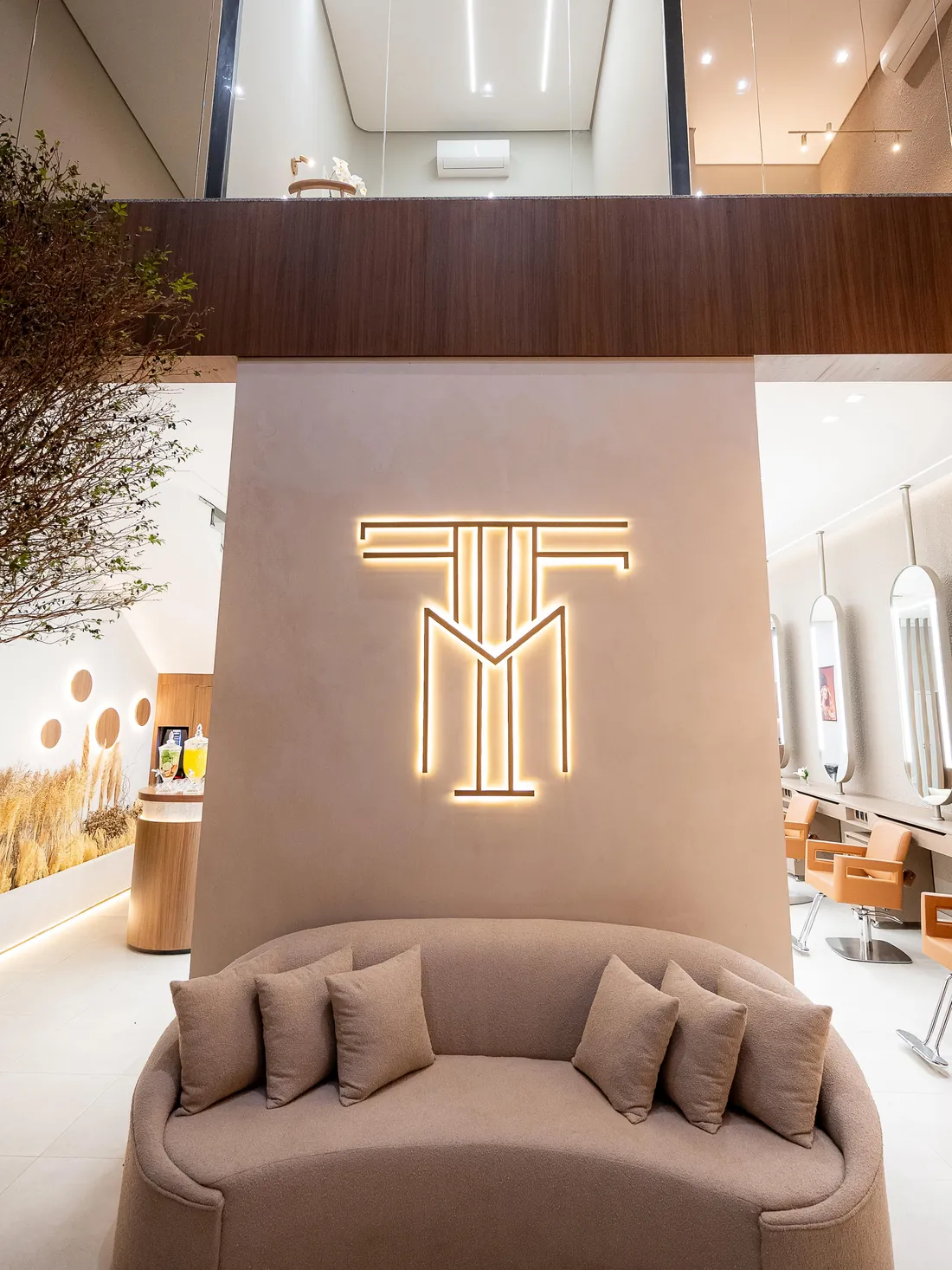 Recepção com o monograma TM iluminado em dourado sobre um sofá curvo