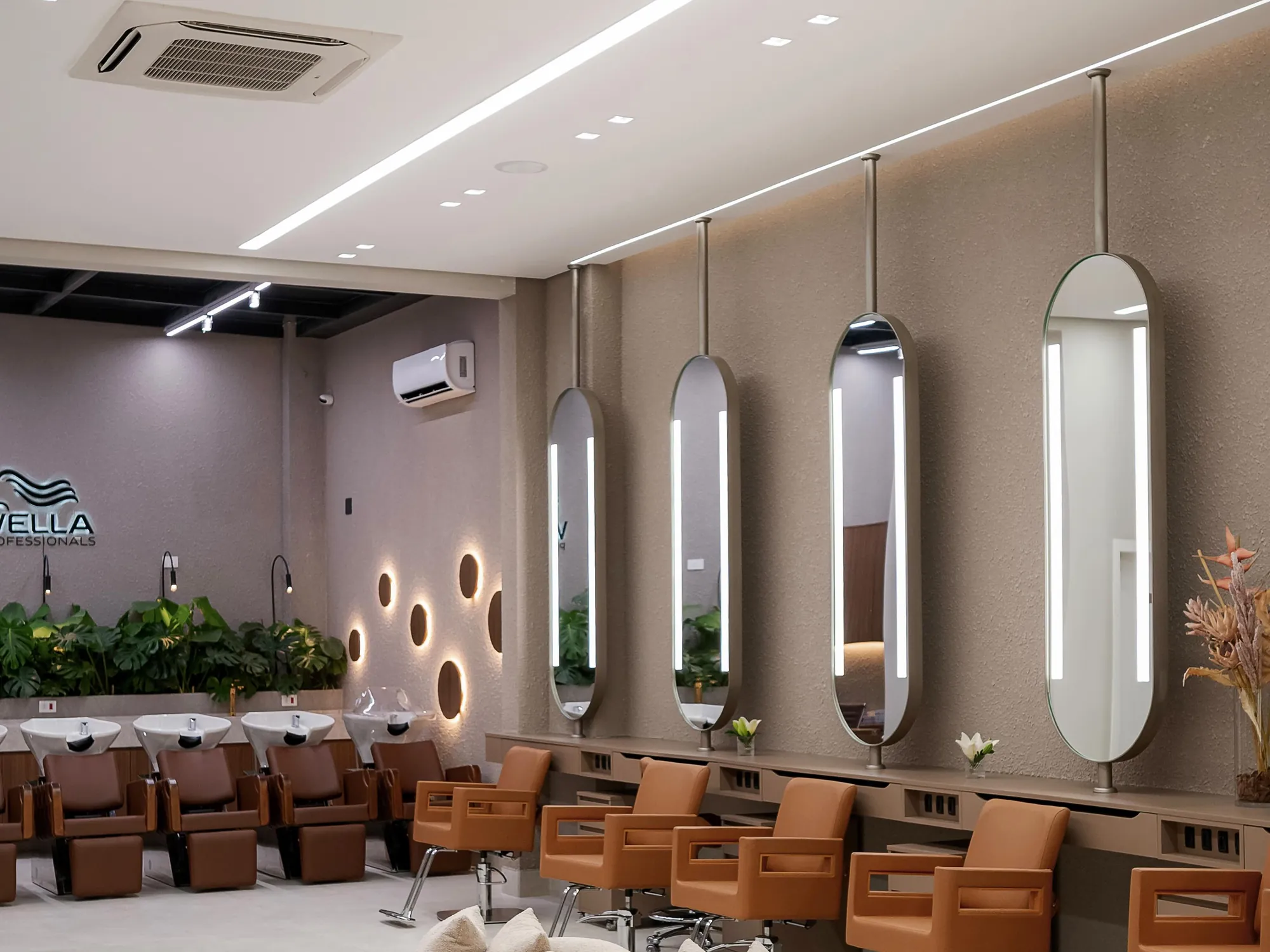 Salão principal com espelhos ovais iluminados, cadeiras de couro caramelo e sofá curvo