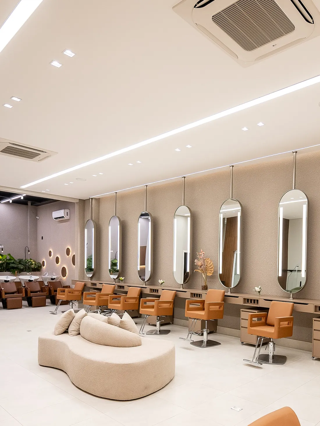 Salão com espelhos ovais de luz e sofá bouclê ao centro